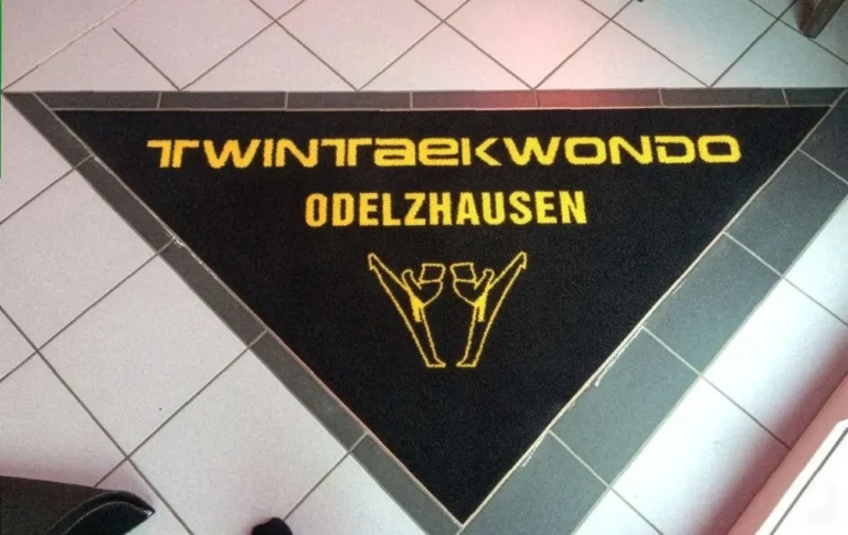 Dreieckige Logomatte mit gelbem Logo und Schriftzug in Bodenaussparung eingepasst